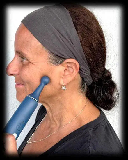A woman pressing the PhysioJaw ball tip against her cheek over the masseter muscle